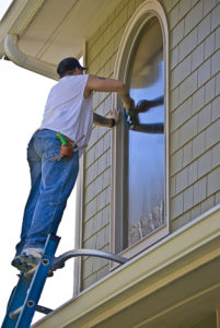 Man on a tall ladder cleaning the window on a house.